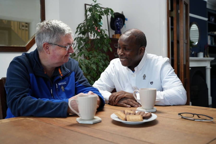 Two men chatting happily while eating biscuits and drinking tea.