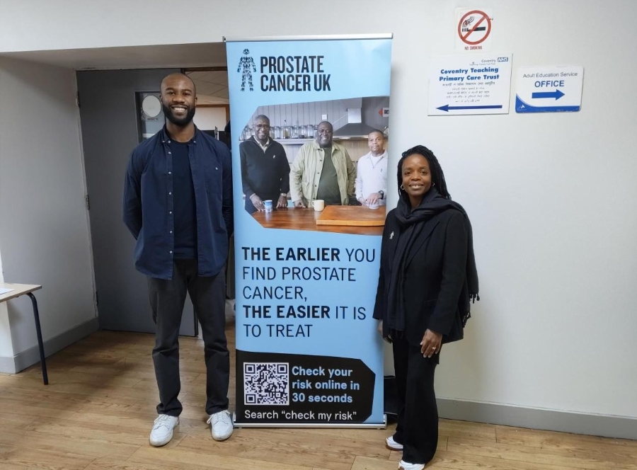 Two members of our Black Health Equity team standing in front of a sign that encourages men to check their prostate cancer risk.