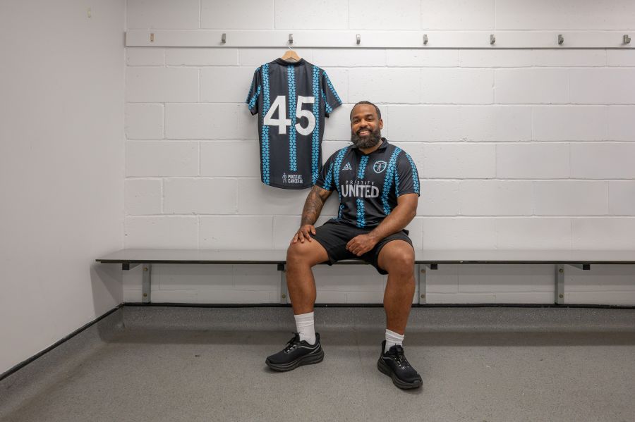 Romaine wearing a Prostate United top sitting on a locker room bench in front of another kit top.