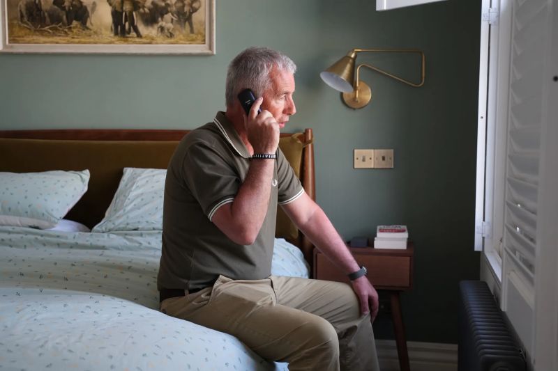 A man sitting on a bed speaking on the phone.