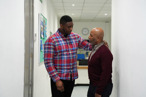 A son consoling his dad with an arm on the shoulder in a clinic.
