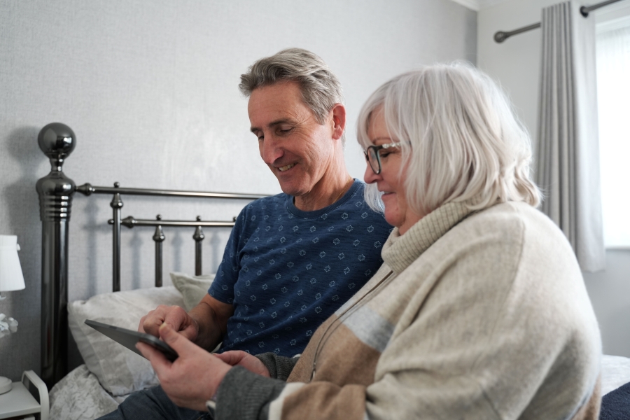 A husband and wife smiling and looking at a tablet screen together.